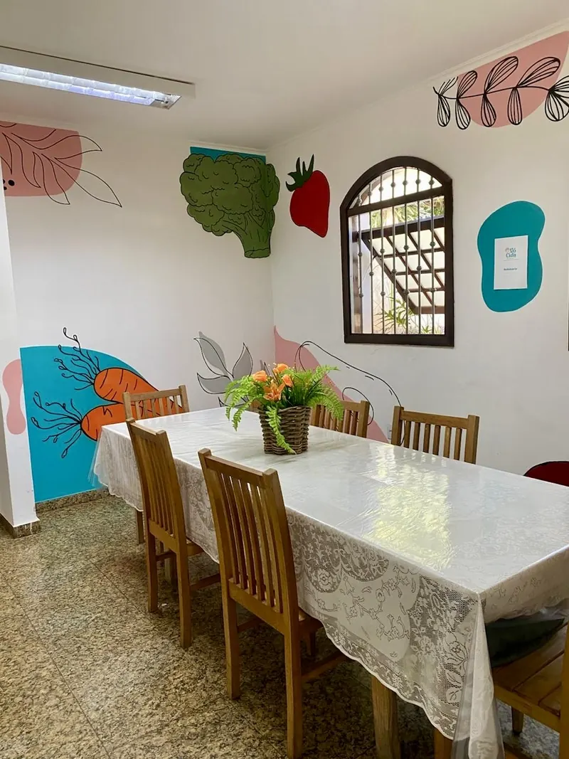 Mesa de jantar longa com toalha de renda em sala com desenhos de vegetais nas paredes