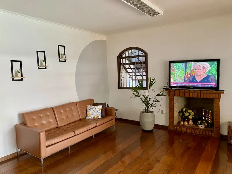 Sala de estar interna com sofá de couro, lareira e TV ligada