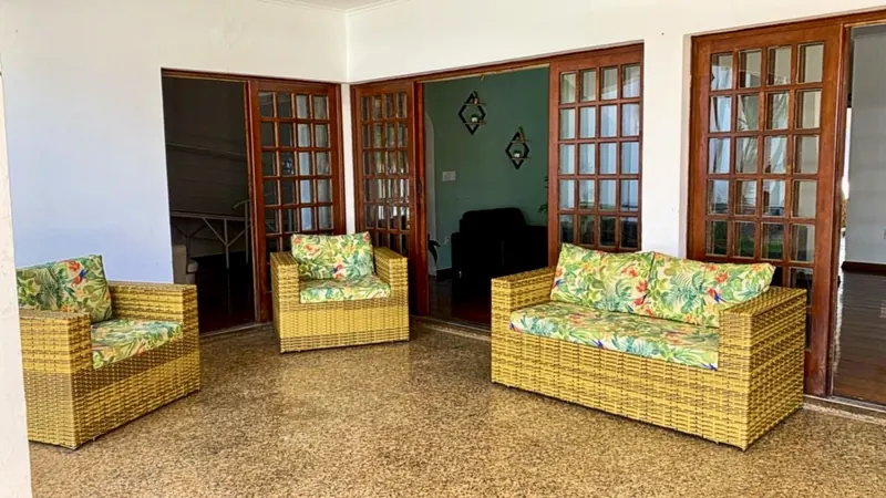 Área externa coberta com sofás de fibra sintética e almofadas florais
